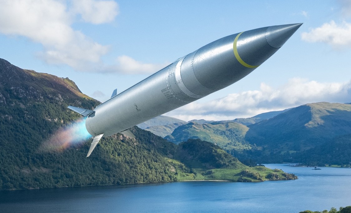 A missile with a yellow band is launched over a scenic landscape with green hills alake and partly cloudy skies
