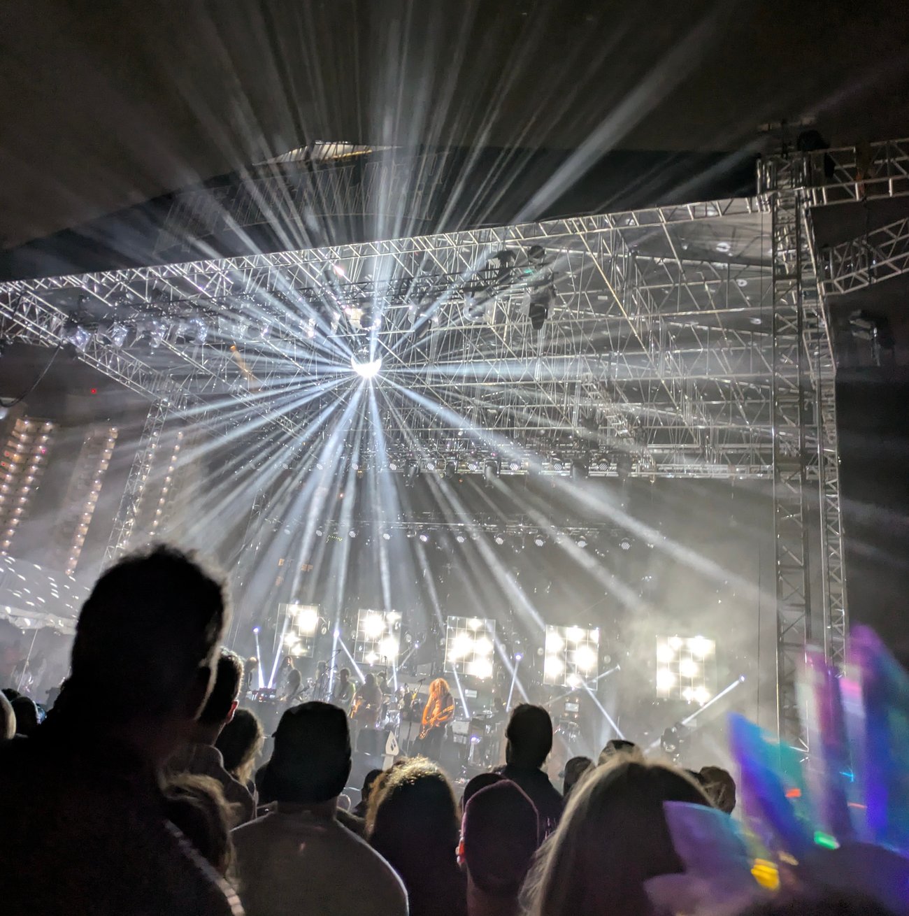 Crowd watching a live concert with bright stage lights radiating over the audience at night.
