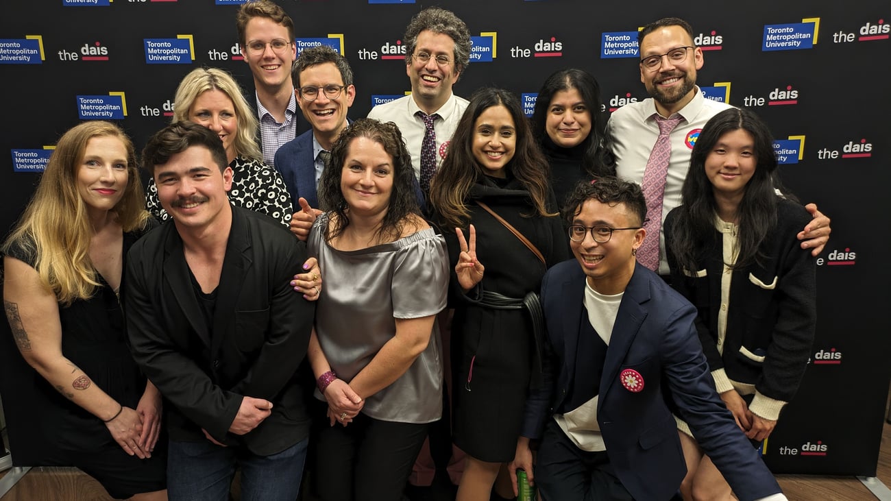 A team photo of employees smiling in front of a Dais backdrop