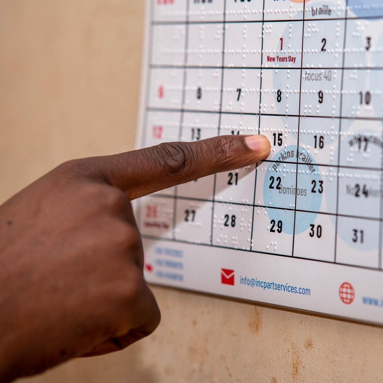 Close-up of a hand reading the January page of an accessible wall calendar that combines printed numbers with braille.