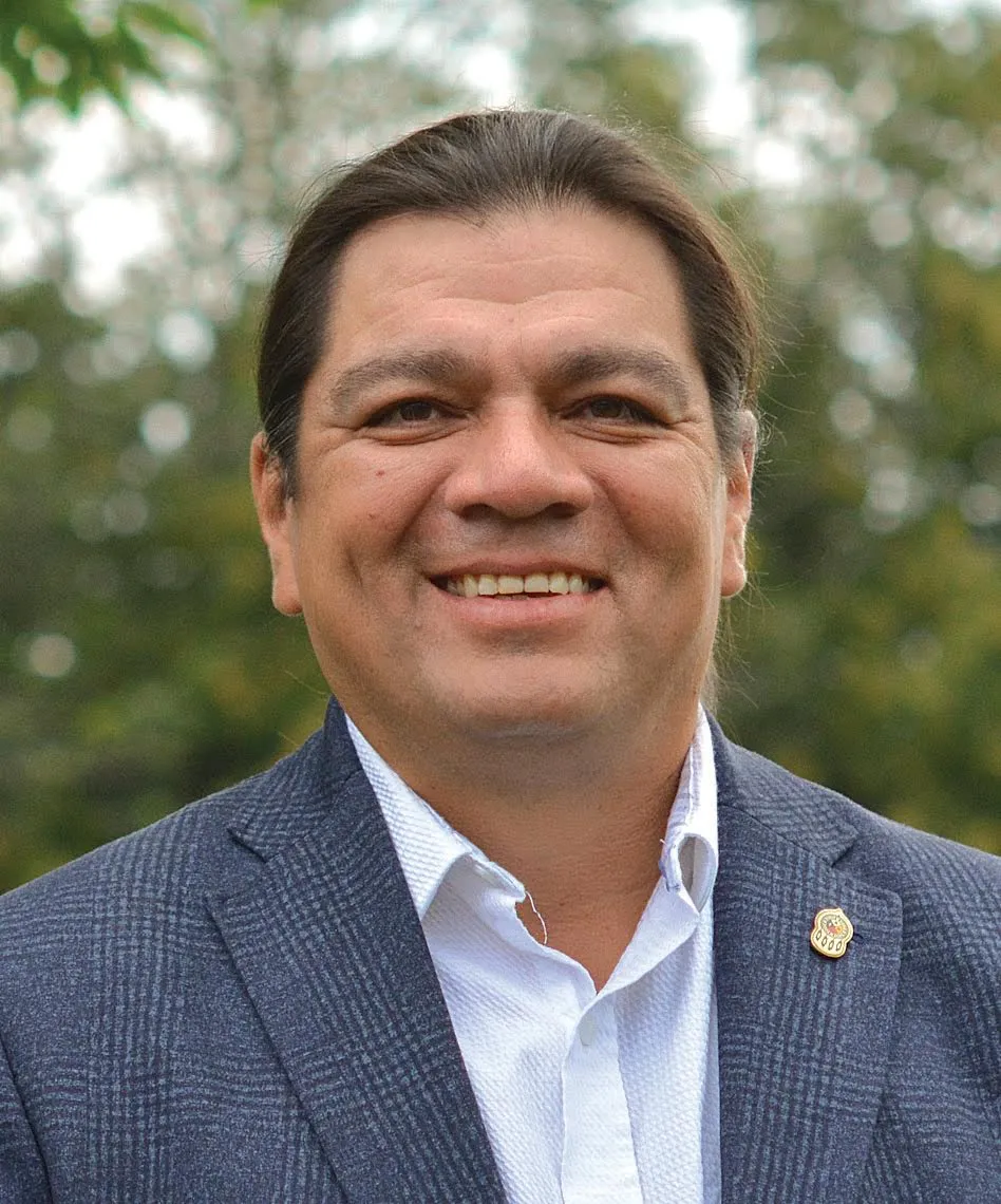 Duke Peltier, smiling against a background of trees and sky.