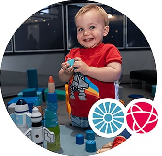 A toddler smiles while playing with a toy rocket.