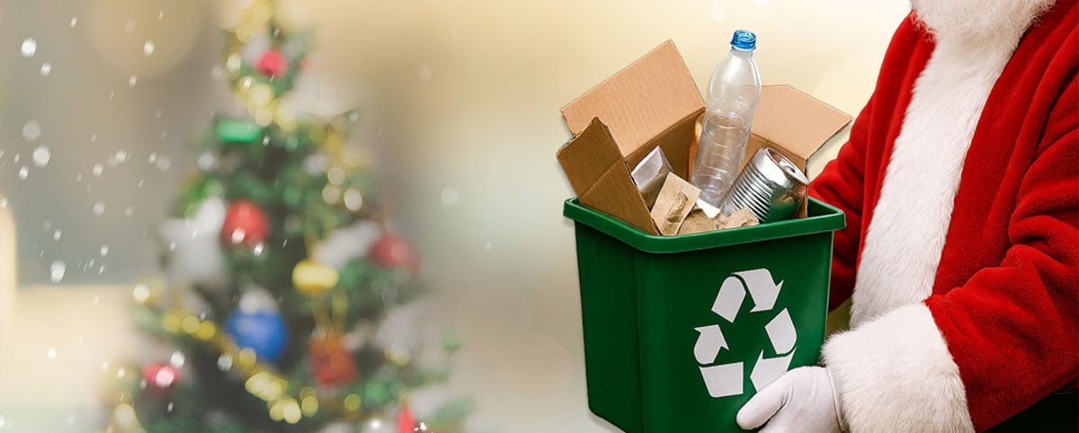 santa holding a bin filled with recycling items in front of a winter christmas tree scene