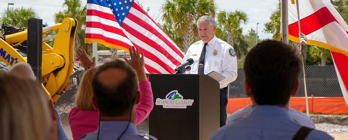 fire chief standing at groundbreaking ceremony podium in front of new station construction site crowd fire chief standing at groundbreaking ceremony podium in front of new station construction site crowd