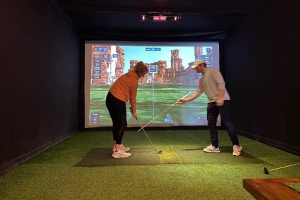 a golf instructor with a female golfer at a simulator