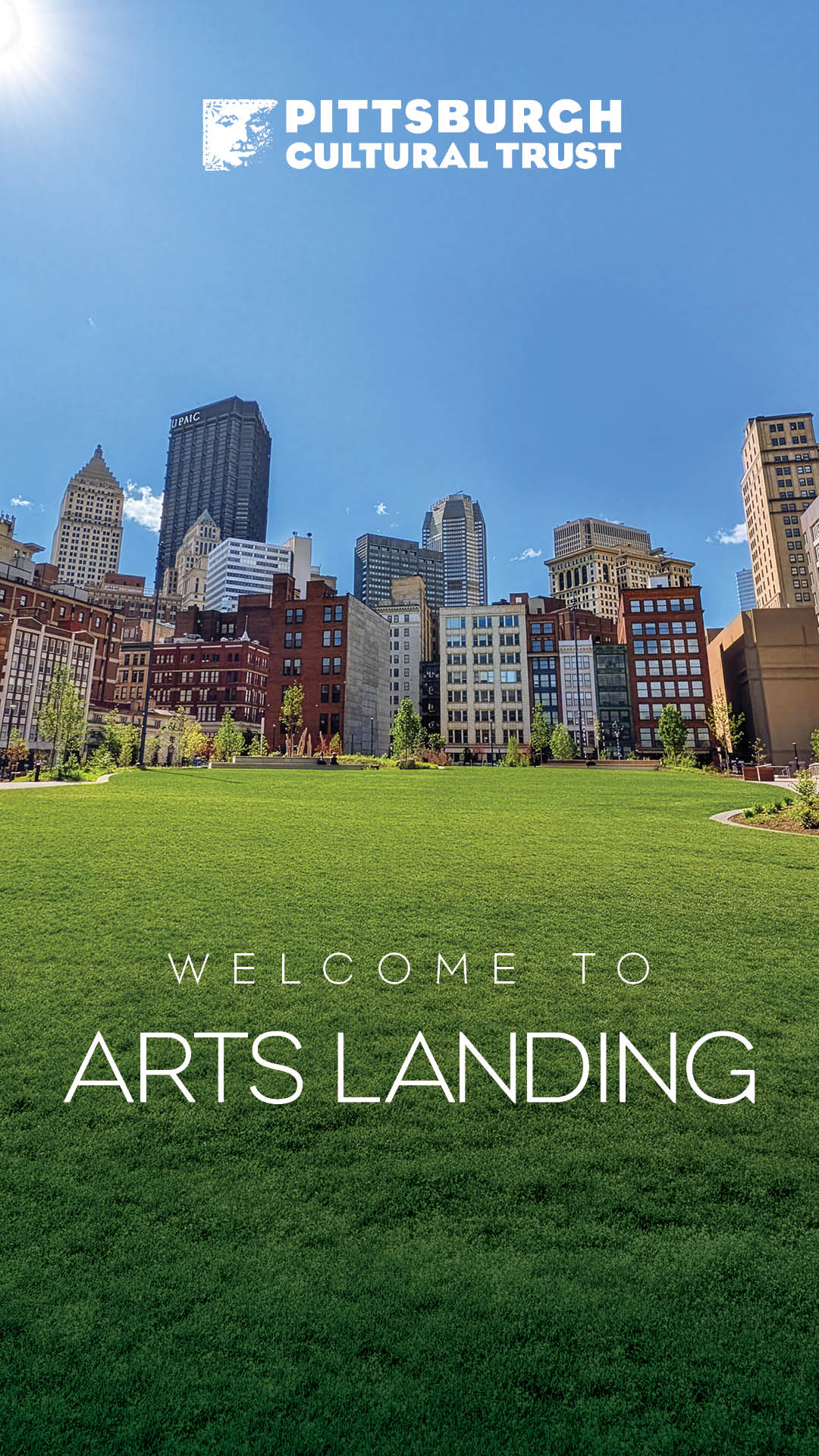 A wide green lawn with modern city buildings in the background under a clear blue sky. White text reads Welcome to Arts Landing.