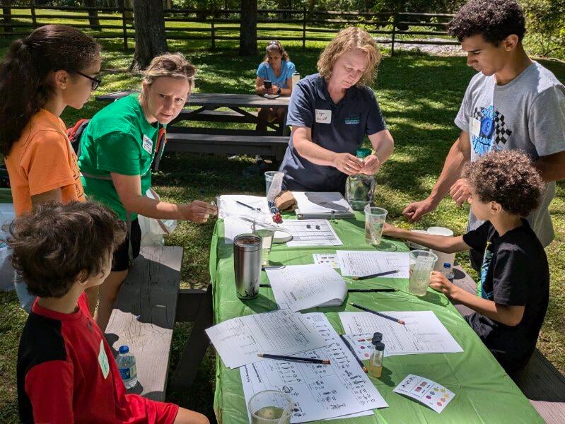 Four Stanly 4-H'ers and two instructors gather around a park picnic table conducting water quality tests.