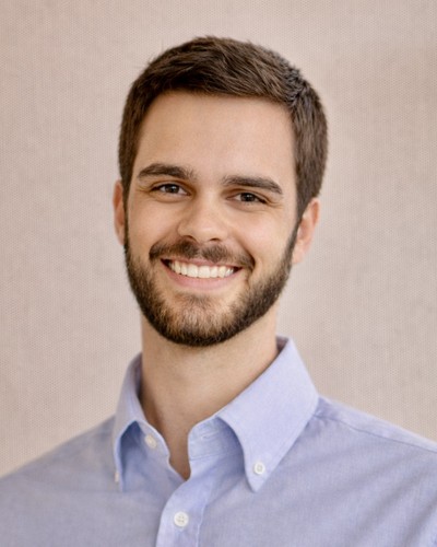 Dalton Suits Extension Agent, Agriculture - Livestock, Equine, Field Crops, and Forages is wearing a blue shirt, smiling. He has a brown mustache and beard with brown hair with a neutral background. 