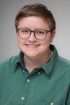 Sydney Blair, 4-H program Assistant wearing a green shirt, glasses smiling with a neutral background. 