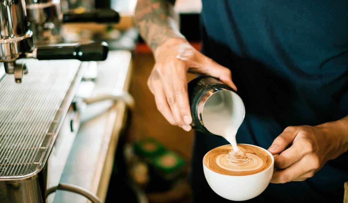 Barista pouring milk into coffee mug
