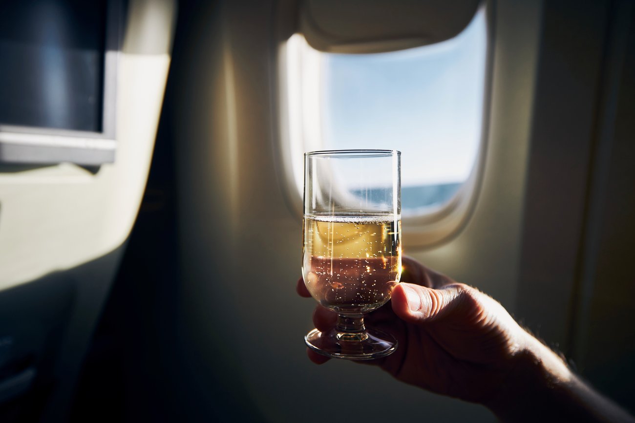 A airplane passenger hold a glass of alcohol near the airplane window.