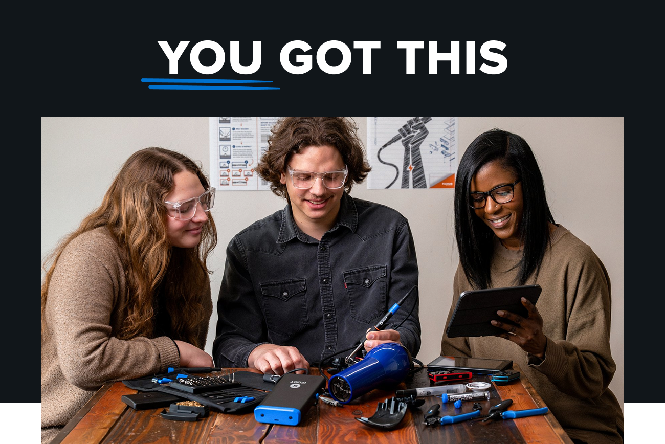 Text: You got this. Graphic: Three people wearing safety glasses work together at a wooden table, repairing a blue hair dryer using iFixit tools while following instructions on a tablet.