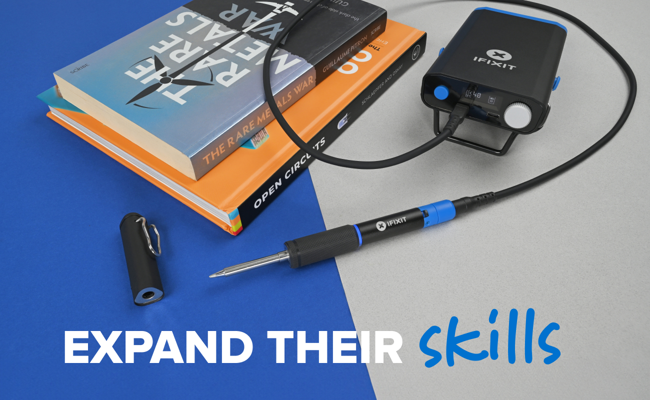 The iFixit FixHub Portable Soldering Station set up on a blue and gray background beside a stack of books, with the soldering iron connected and its magnetic cap placed nearby. White and blue text reads “EXPAND THEIR skills,” highlighting learning and creativity through hands-on repair.