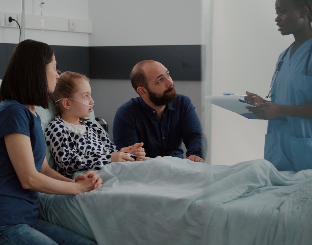 Photo of a mom, dad, and a child in a hospital bed talking to a healthcare provider. 