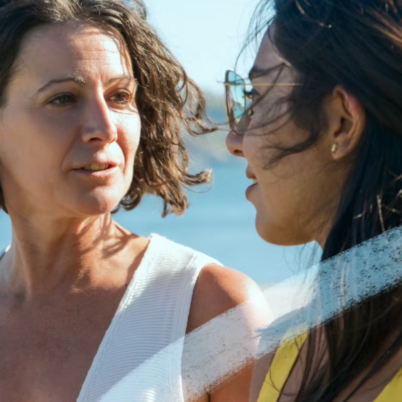 Two women talking to one another with the ocean behind them