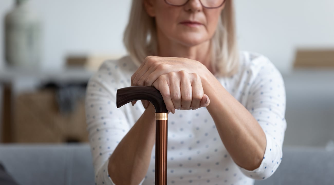 Image of a woman sitting down, holding onto a walking cane