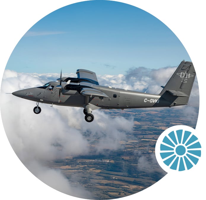 A twin-engine grey aircraft flies above the clouds, with farmland visible below.