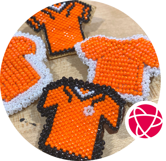 Four orange beaded pins in the shape of a t-shirt. 