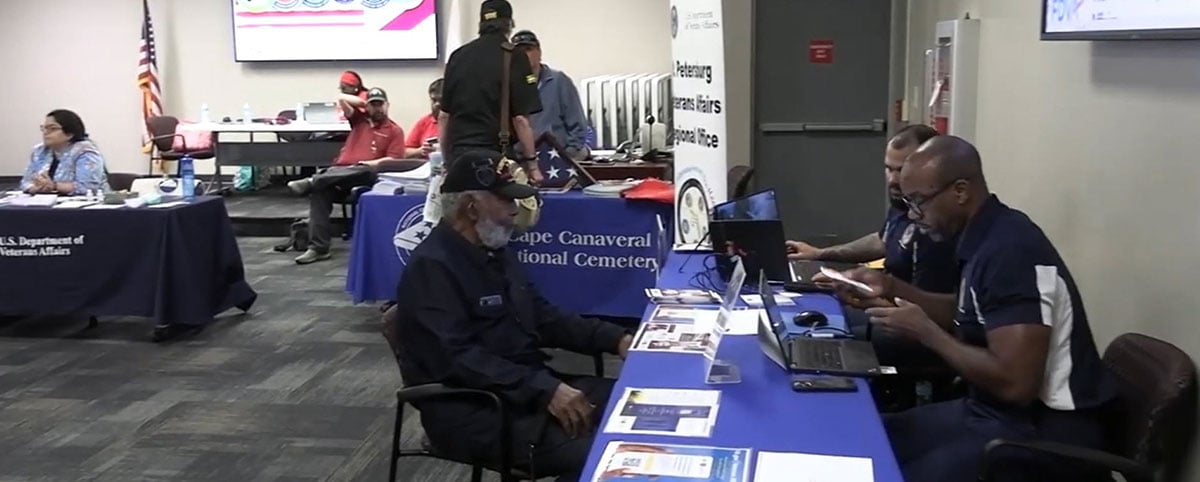 veteran at table surrounded by event volunteers helping veteran at table surrounded by event volunteers helping