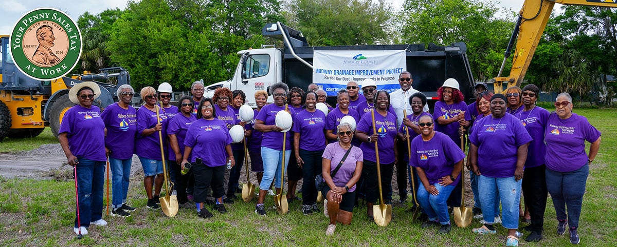 group of people holding shovels standing in front of groundbreaking site and equipment, penny sales tax logo in corner group of people holding shovels standing in front of groundbreaking site and equipment, penny sales tax logo in corner