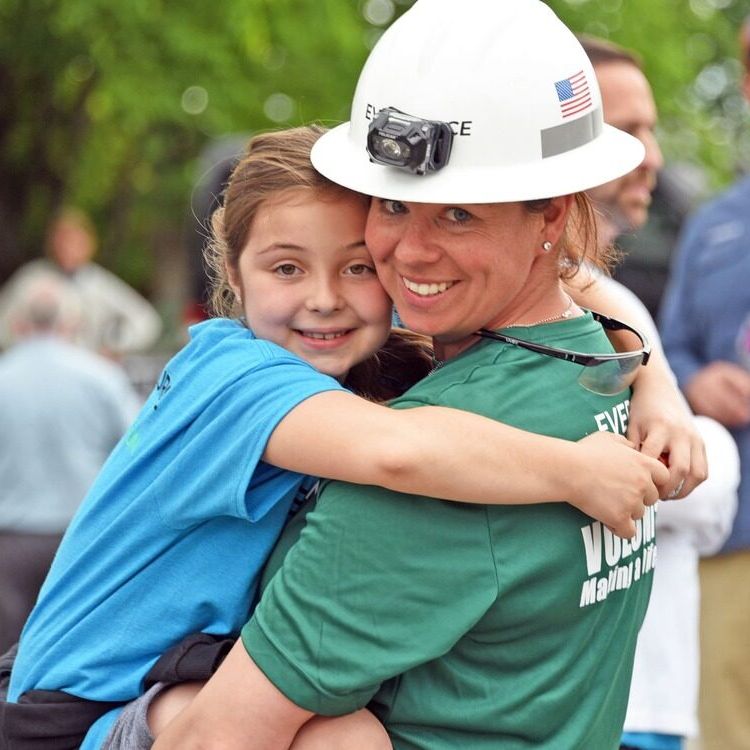 An Eversource staff member holds a young girl in a light blue t-shirt.