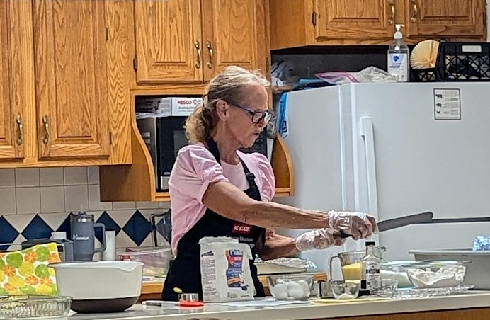 Female volunteer in a kitchen, with recipe ingredients on the counter and she is putting them together in a recipe.