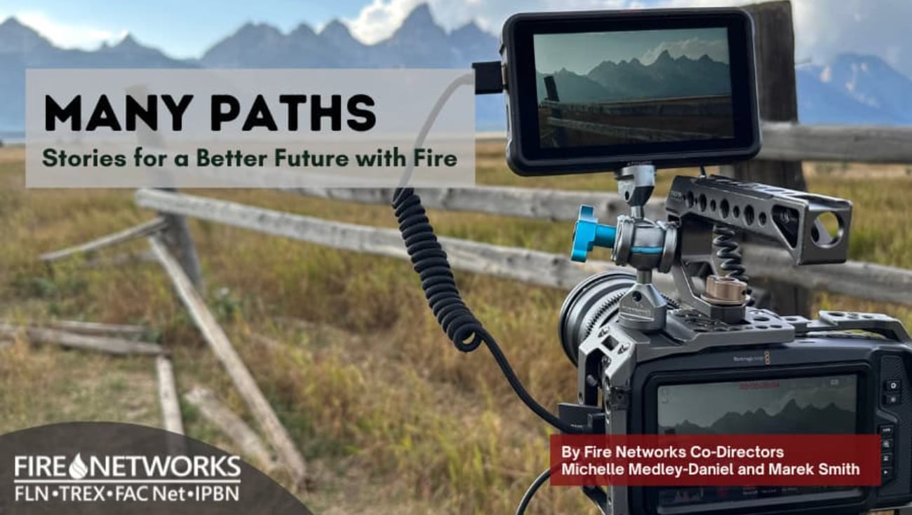 A promotional graphic titled "MANY PATHS: Stories for a Better Future with Fire." The background shows a professional cinema camera rig set up outdoors, filming a scenic landscape of mountains and a wooden fence. A small monitor on the camera displays the shot. In the bottom-left, the Fire Networks logo appears with the text "FLN • TREX • FAC Net • IPBN." A red banner in the bottom-right credits the work to Fire Networks Co-Directors Michelle Medley-Daniel and Marek Smith.