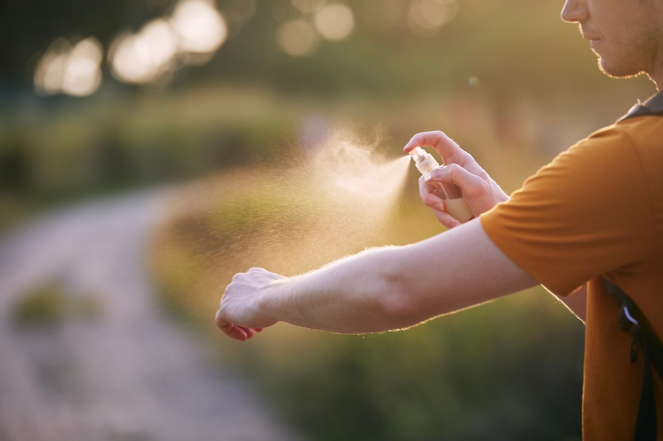 man spraying mosquito repellant to his arm outside