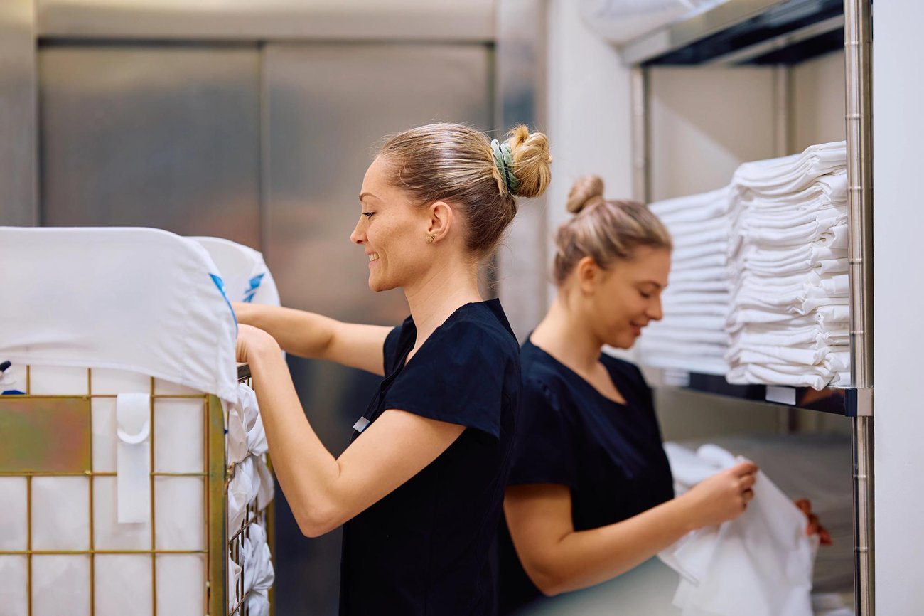 Two maids working in hotel folding towels. They are smiling. 