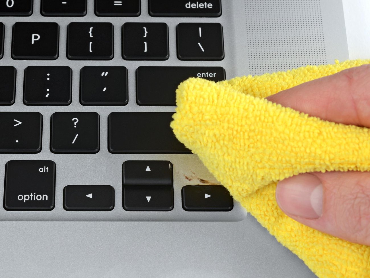 Laptop keyboard with a sticky smudge, being wiped away by a yellow microfiber cleaning cloth.