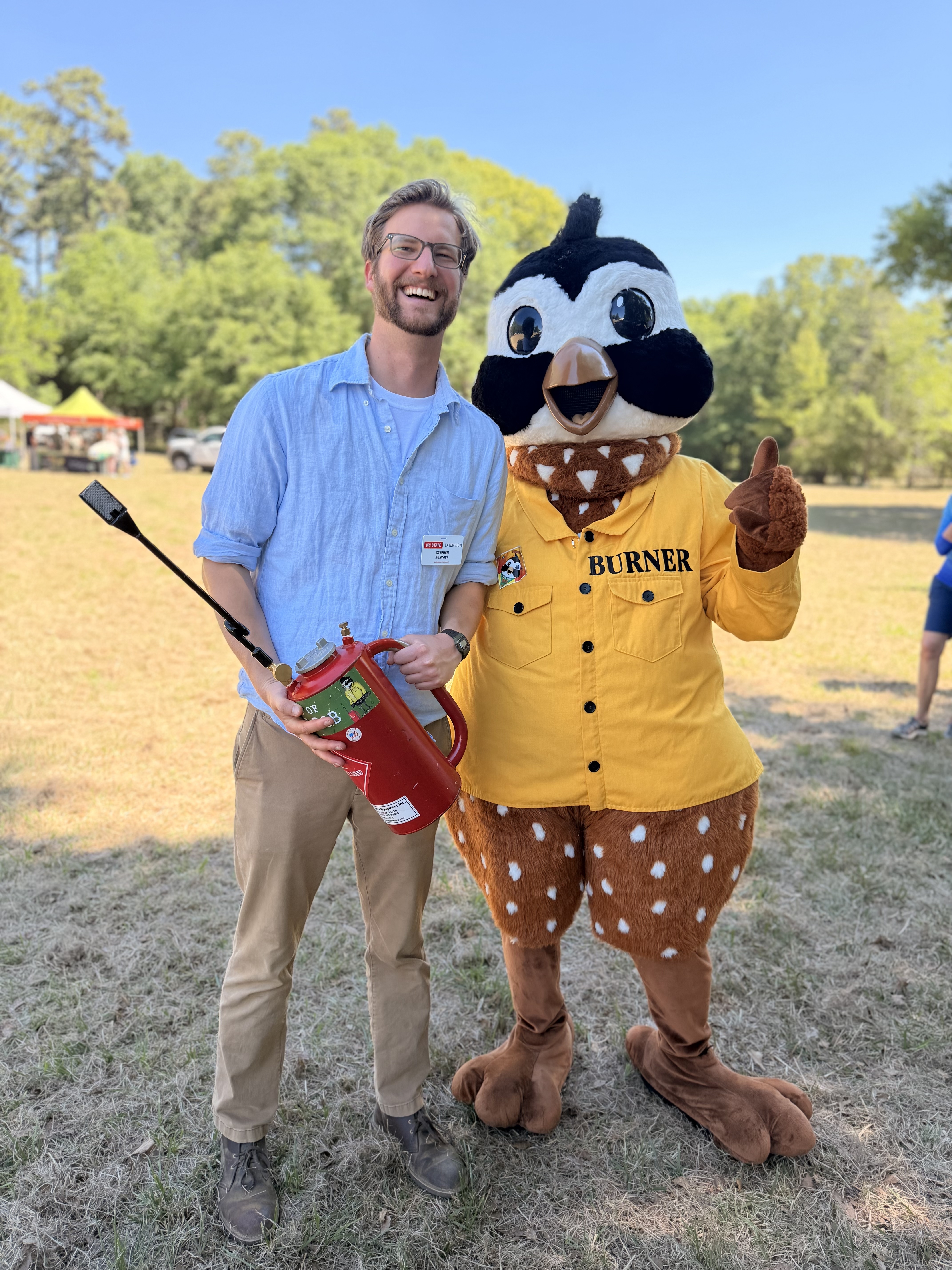 Extension Associate Stephen Ruswick, holding a red driptorch, stands with Burner Bob at the Party for the Pine Fire Festival.