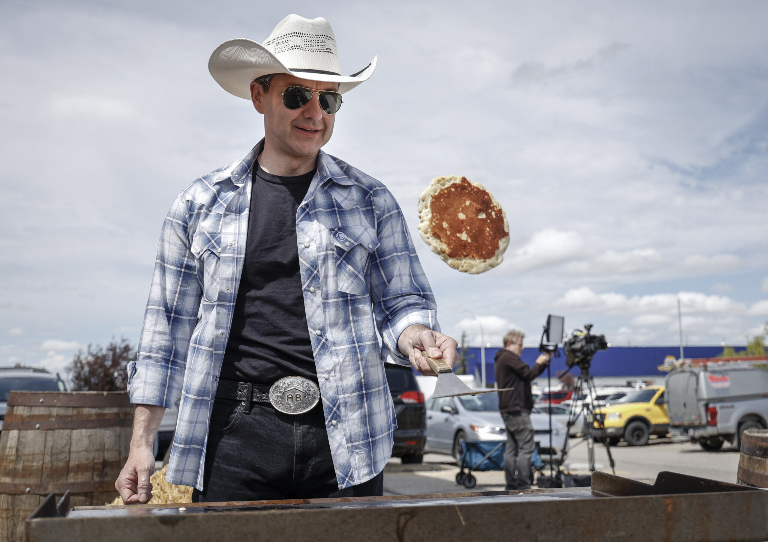 A photo of Pierre Poilievre in casual attire, a hat, and sunglasses, tossing a pancake.