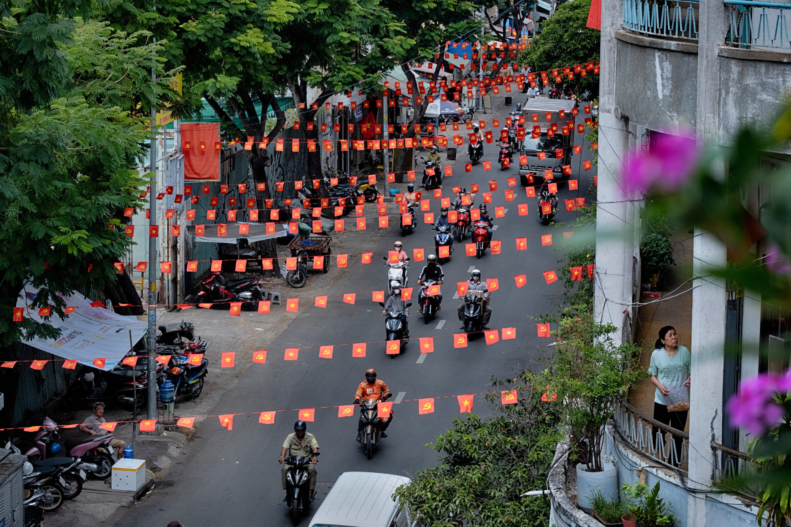 Motorbikes ride along a street under strings of Vietnamese flags.