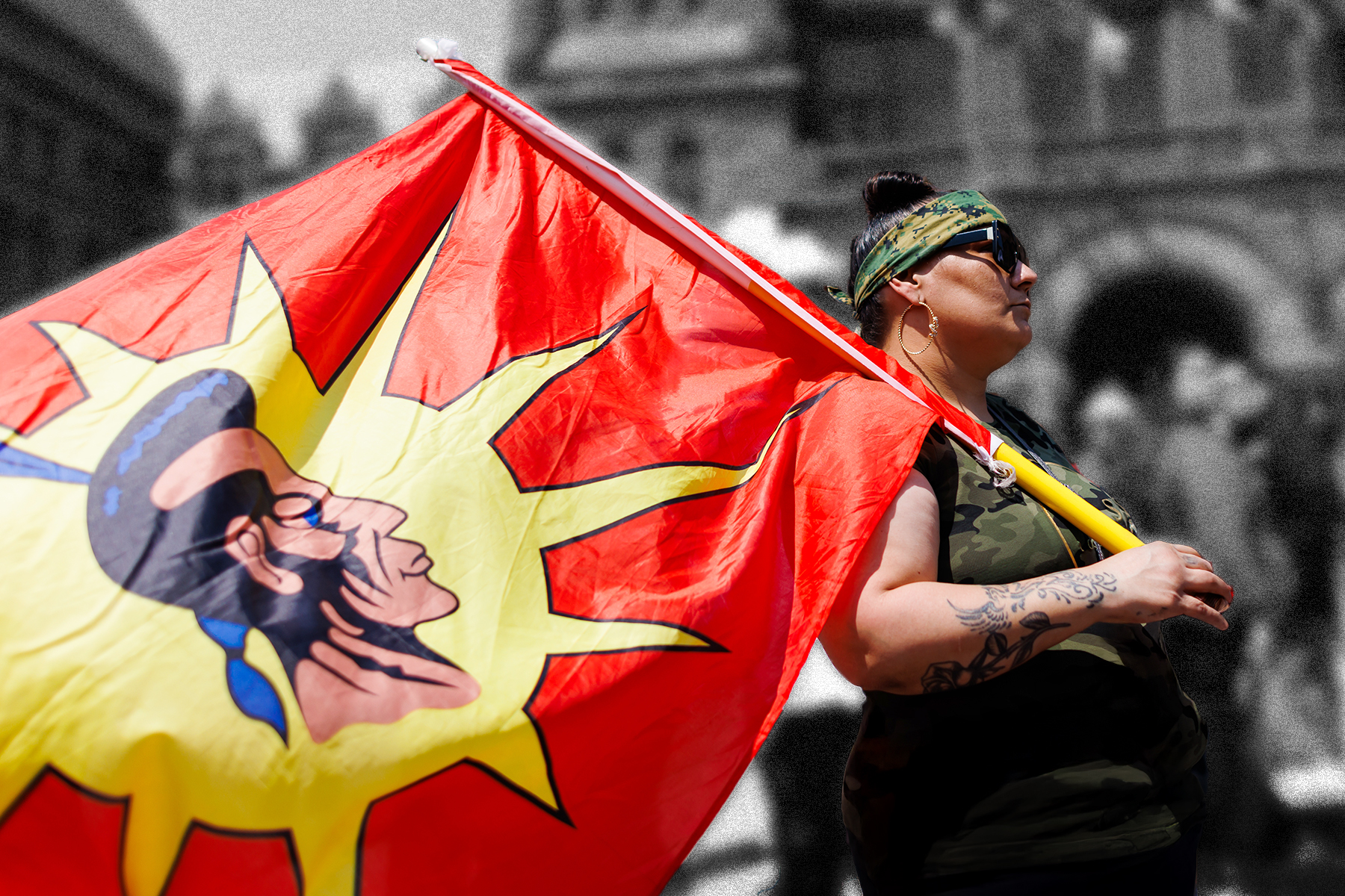 A photograph of a person holding a large red and yellow Mohawk warrior flag. The background is greyed out and blurred.