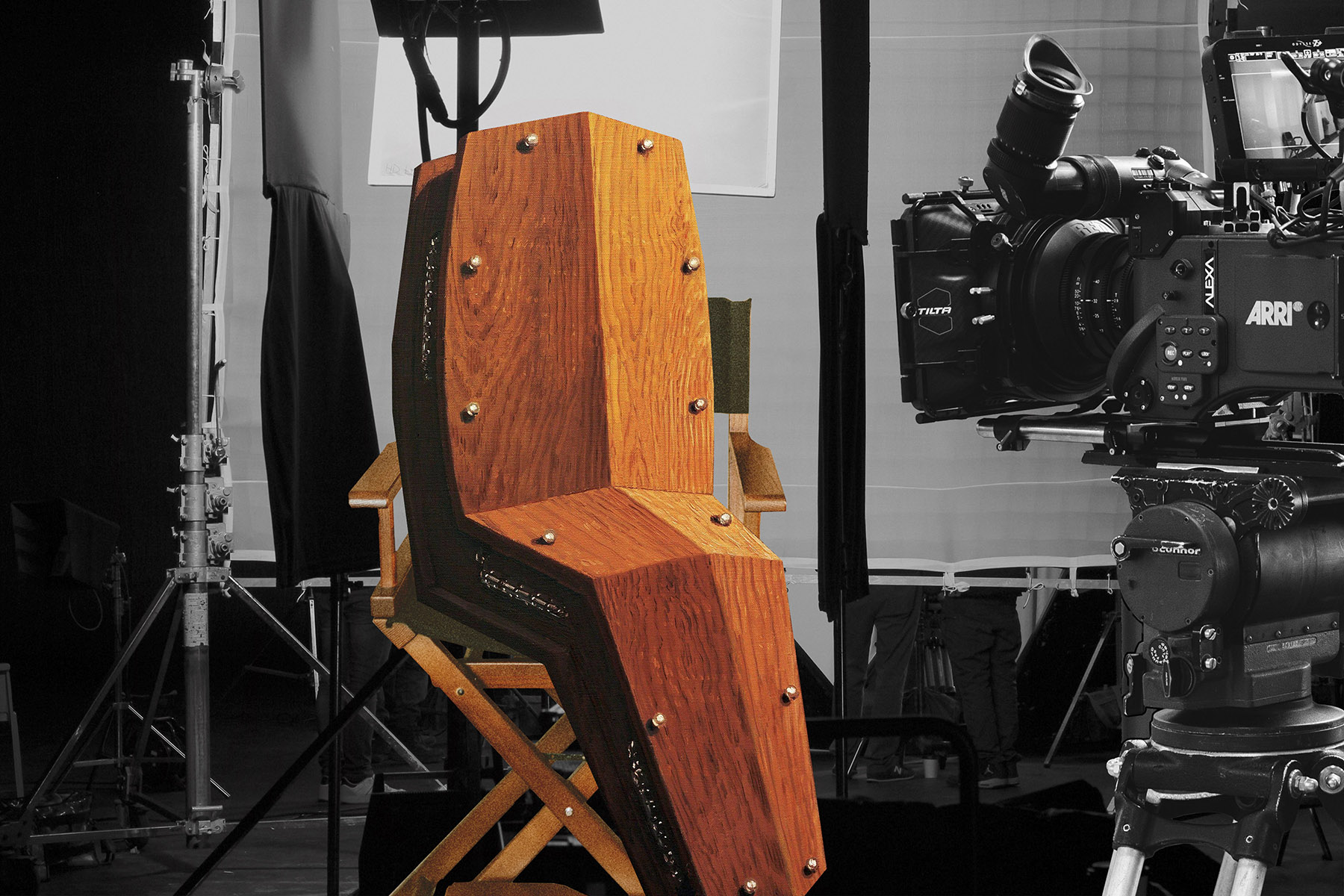 A photo illustration of a wooden coffin in a director's chair facing a video camera.