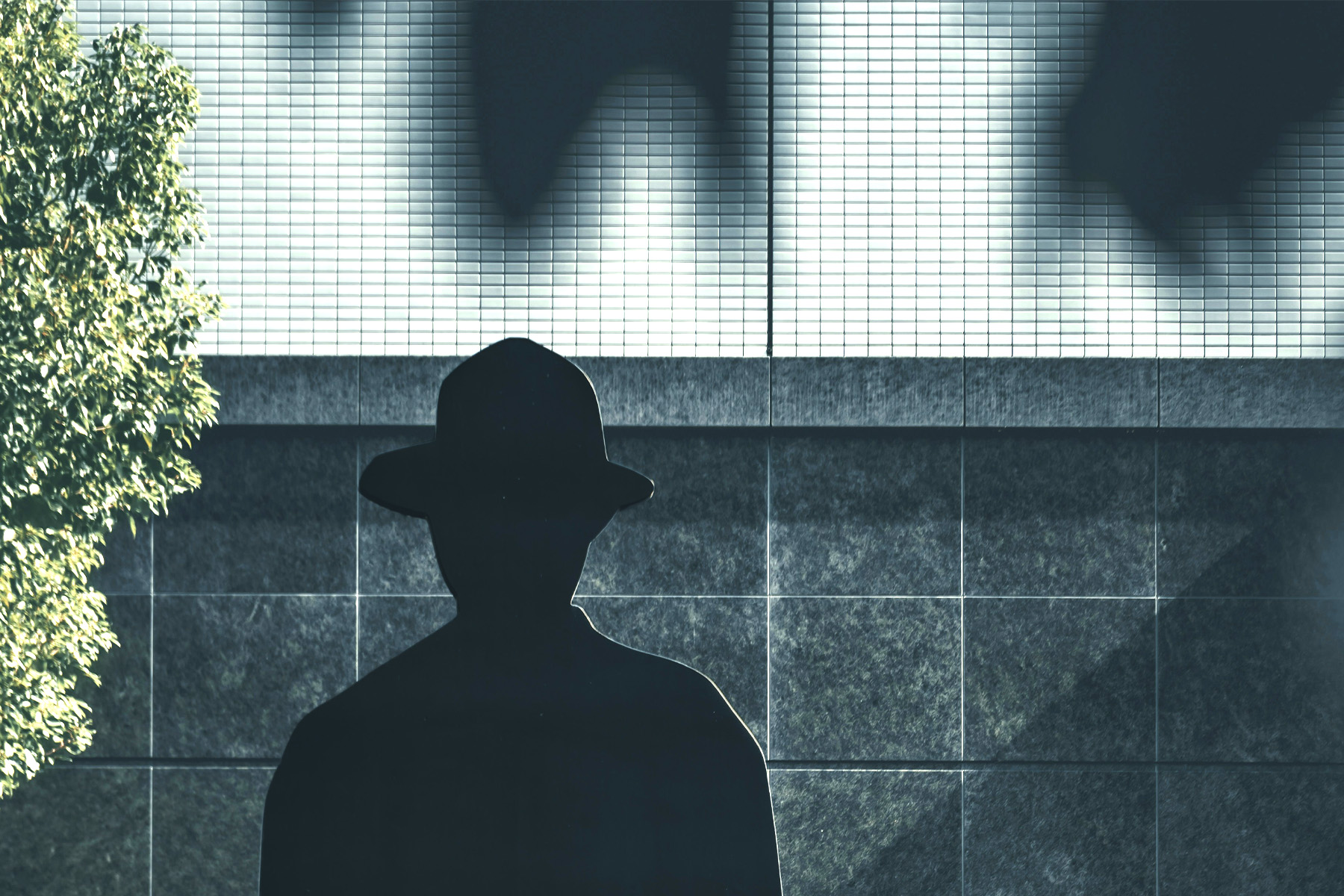 A sillhouette of a man in a hate in front of a shadowy building.