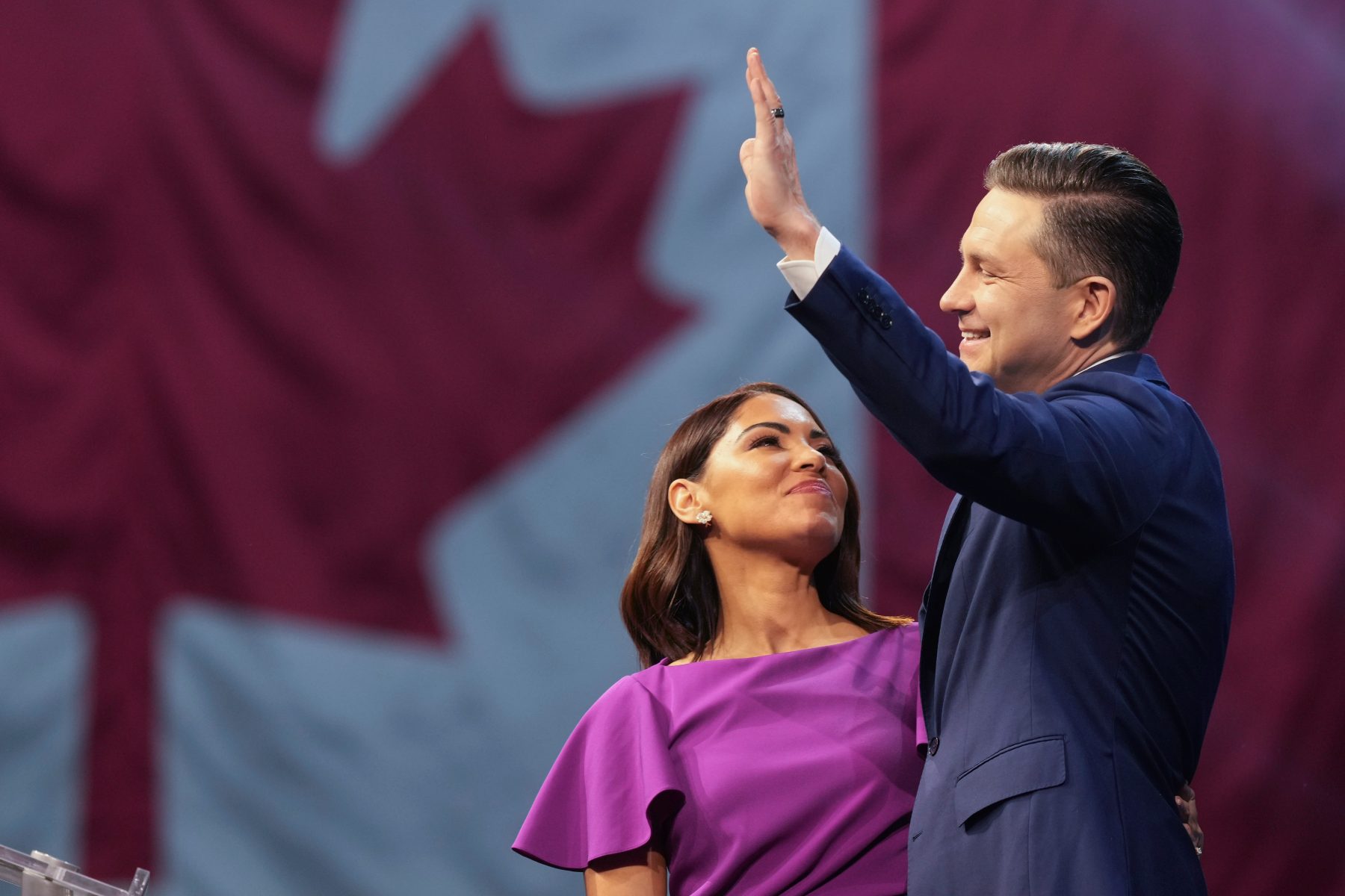 Pierre Poilievre and his wife Anaida at his campaign headquarters on election night in front of a Canadian flag.