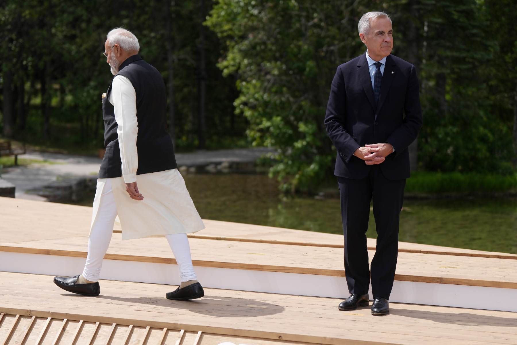 Narendra Modi walks away from Mark Carney, who has his hands folded together and is looking off camera.