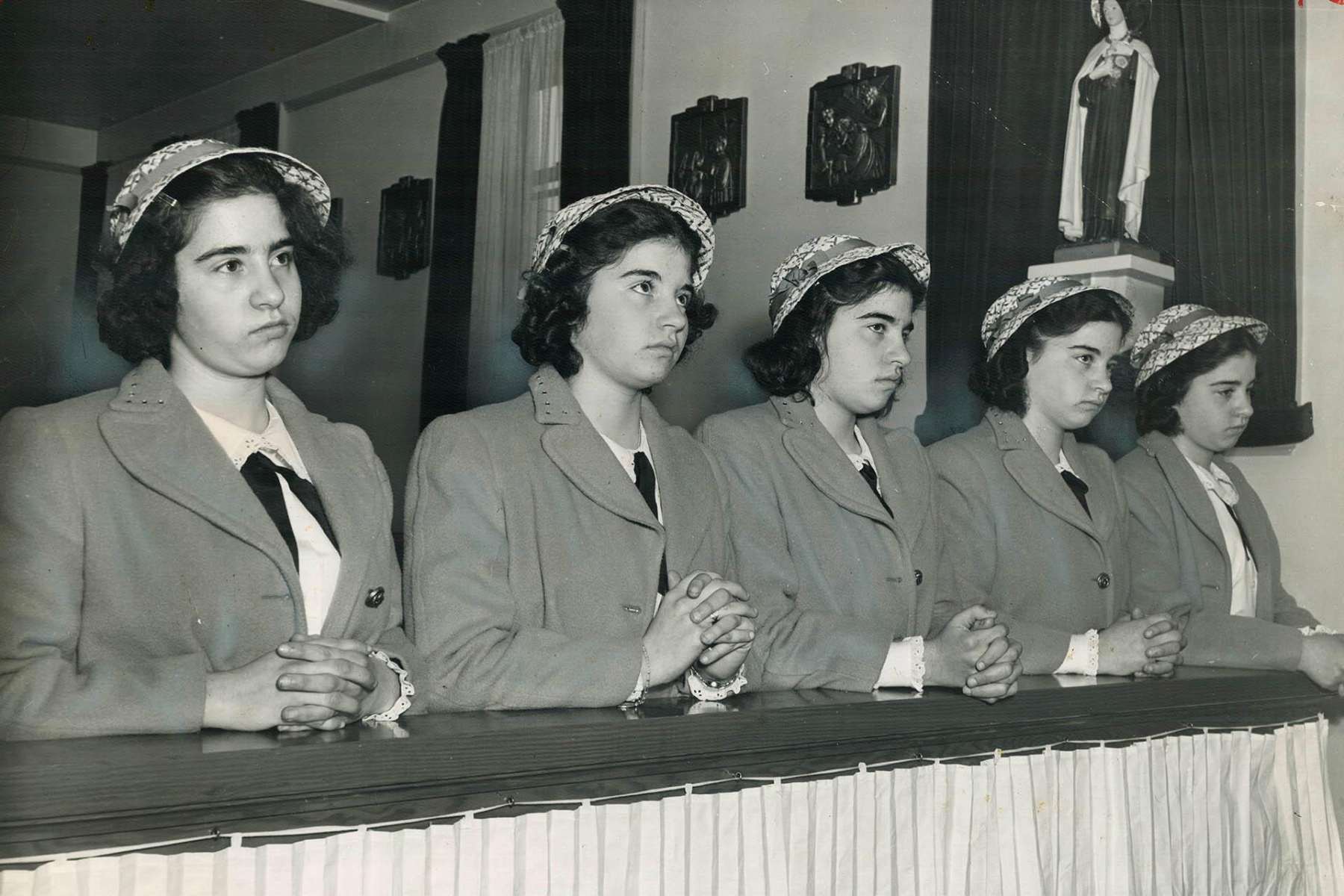 A black-and-white photo of the Dionne quintuplets, five identical teenage sisters, hands folded while kneeling in a pew.
