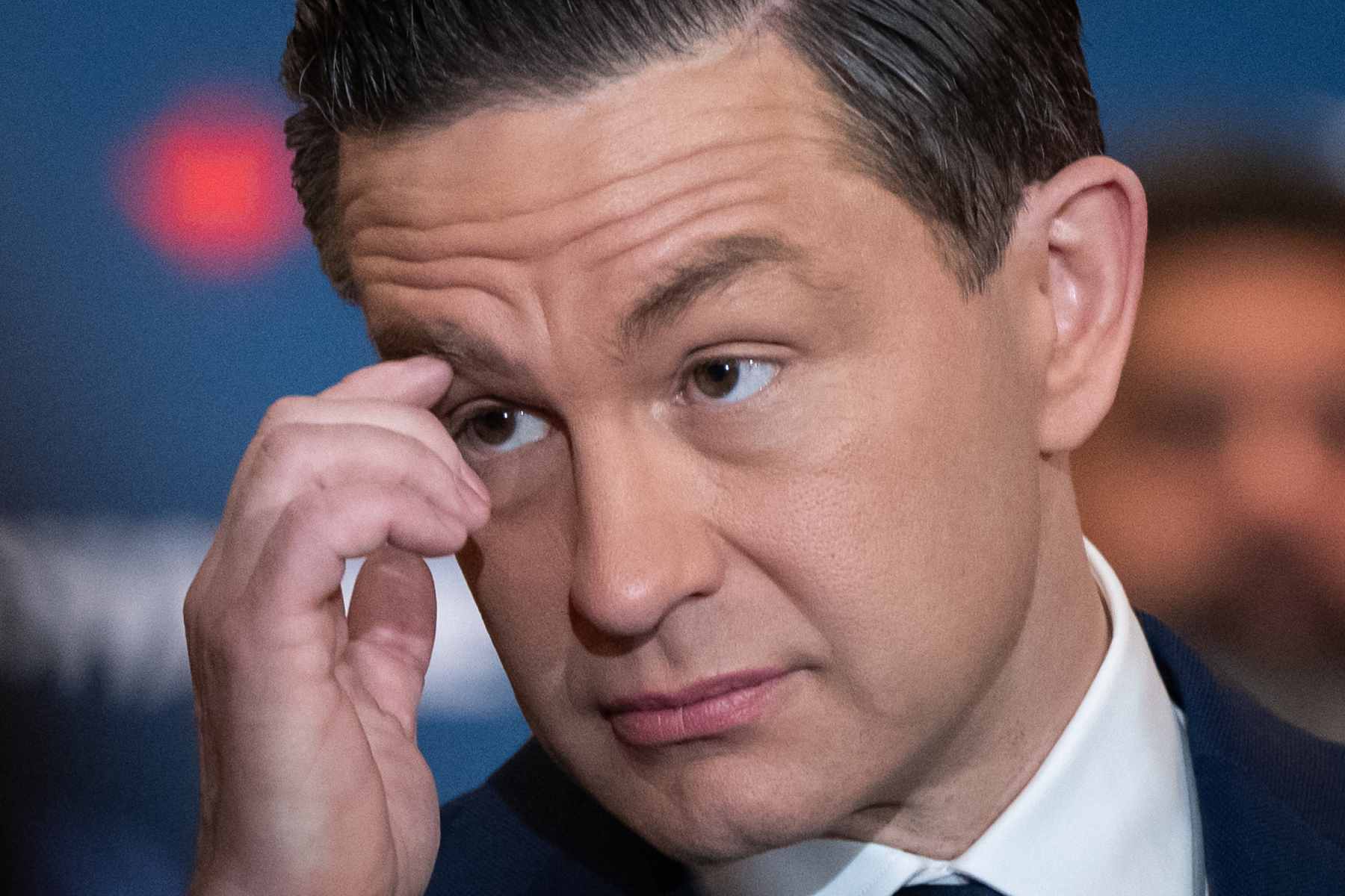 A closeup photo of Pierre Poilievre, wearing a suit and tie, his hand resting near his eyebrow.