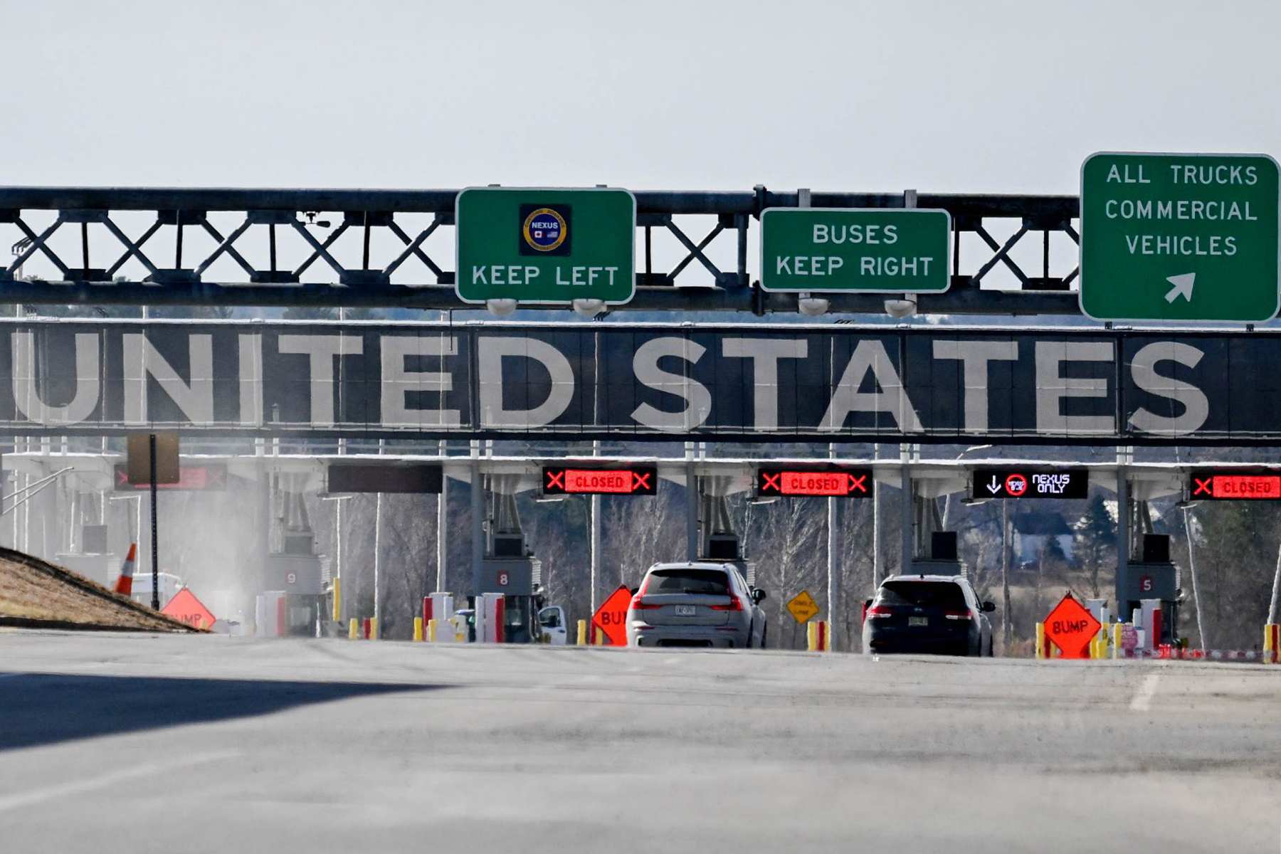Photo shows two cars at a border crossing along a highway, with the words 'United States' and three green signboards looming over them.