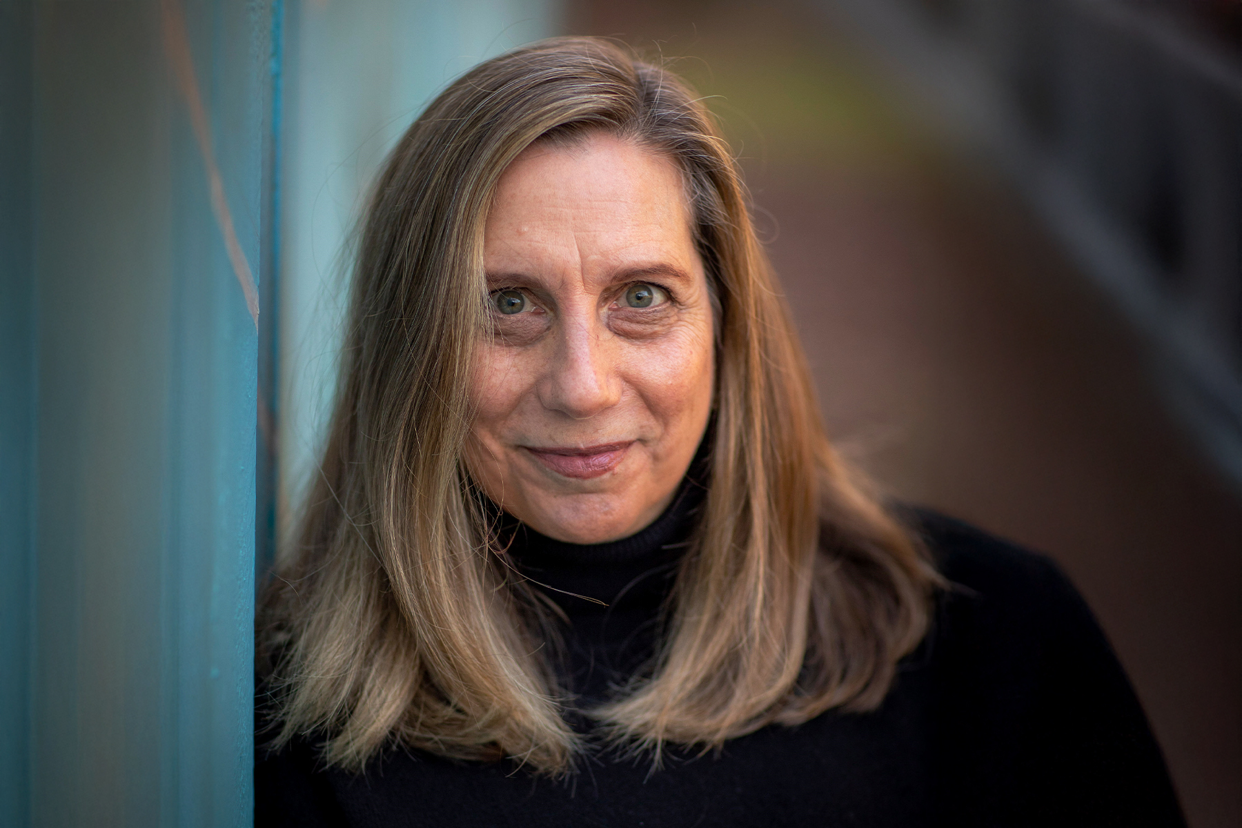 A closeup photo of author Marsha Lederman in a black attire standing against and blue background.