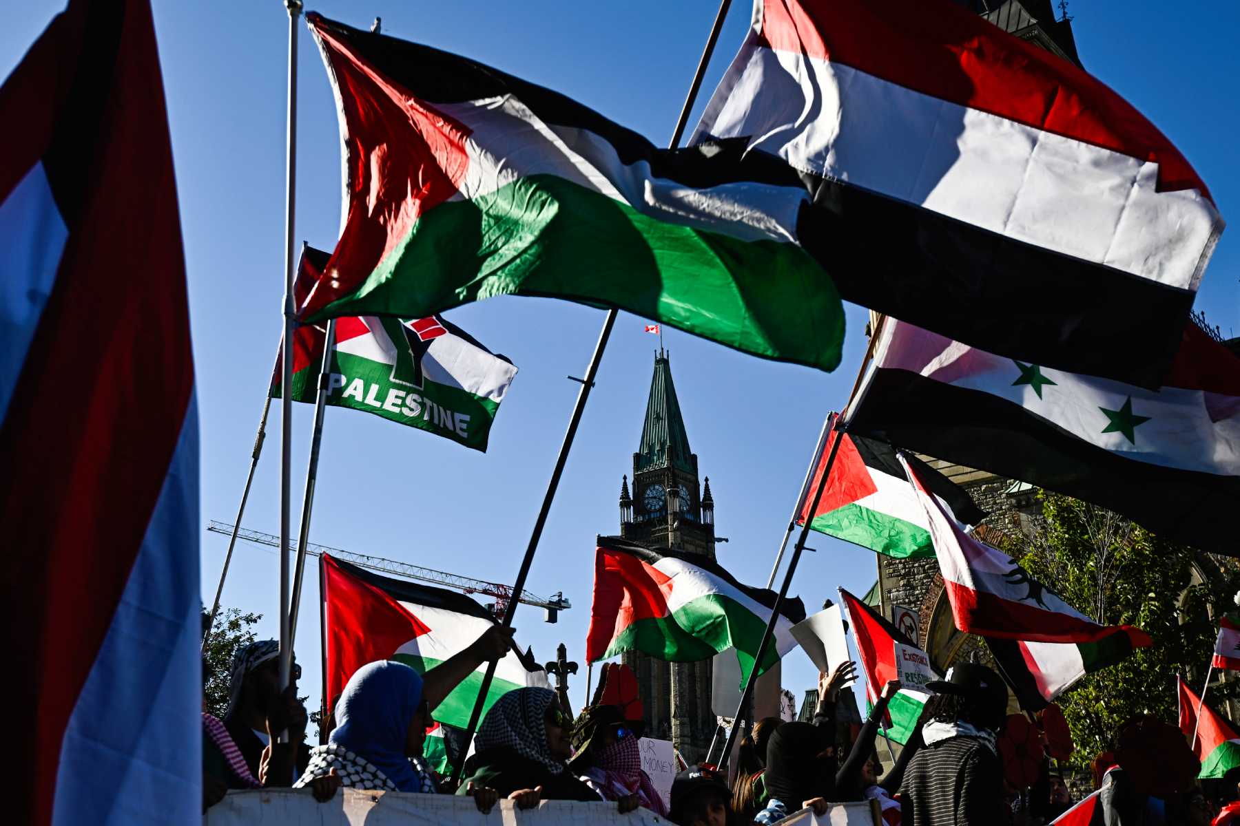 The flags of Palestine and other Arab states are waved in front of a blue sky and the House of Commons in Ottawa.