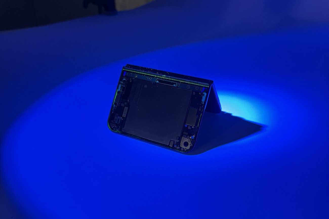 A partly disassembled iPhone Duo standing half-folded under blue UV light, with glowing dust along its frame